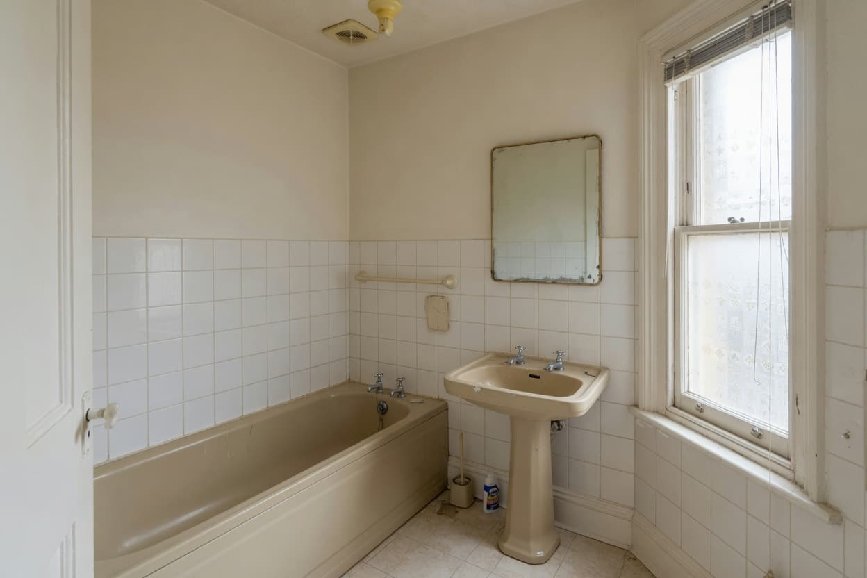 A dated beige bathroom suite with a pedestal basin and tiled walls.